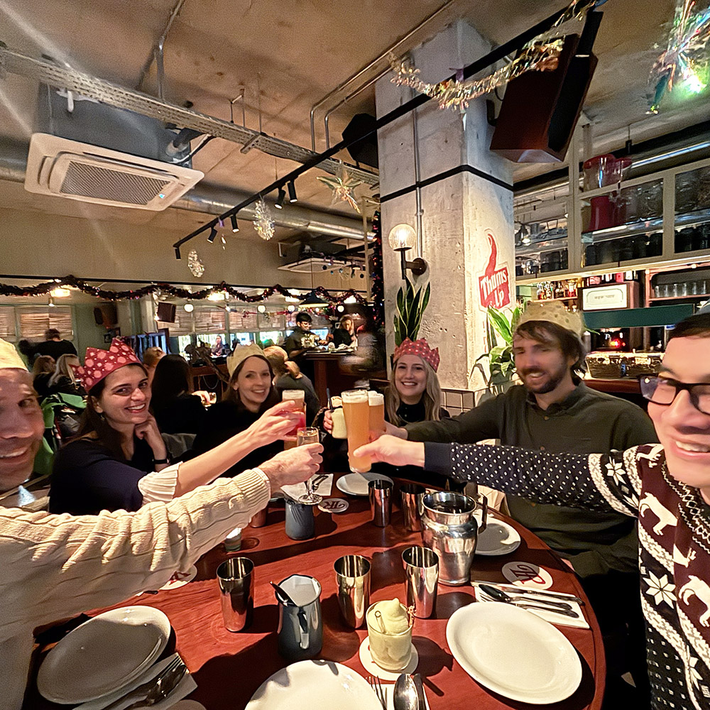 251218 Sow Space Architects Christmas Party_1 Architects and designers sat around a table with drinks and party hats proposing a toast