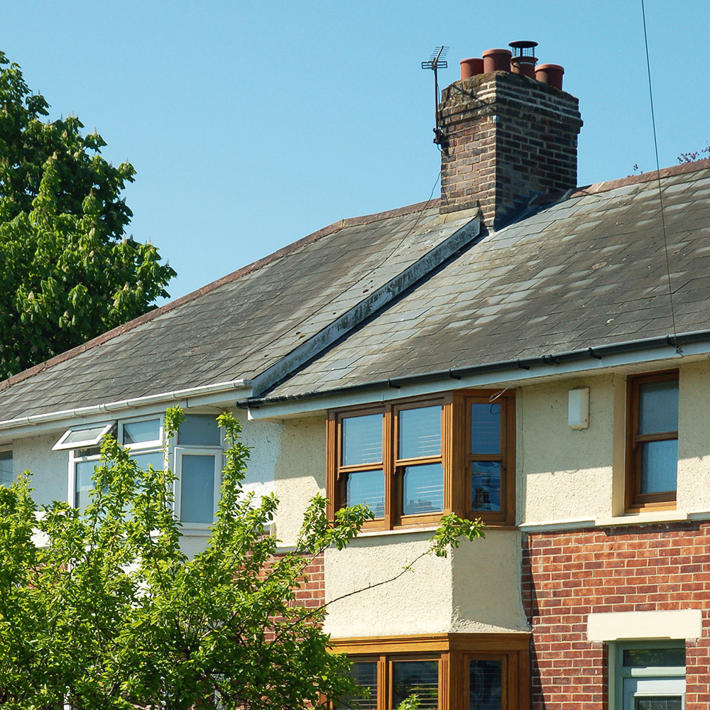 Photo of front of half brick half rendered house, with blue sky above and trees to the side.